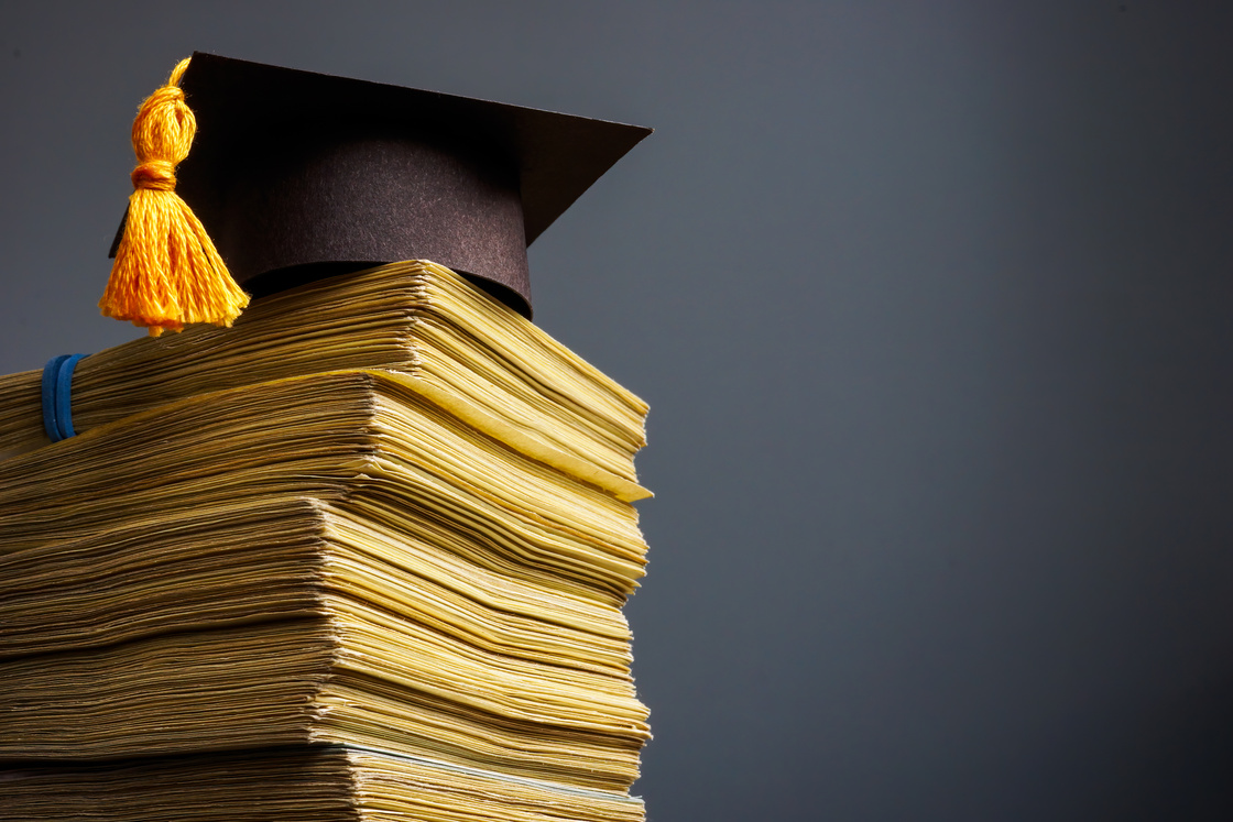 Cost of education concept. Graduation cap and stack of cash for college.